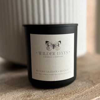 Hand-poured soy candle with X wood wick in a matte black vessel. Woody Brandy & Leather scent with bergamot, leather, tobacco, rosemary, and patchouli by Wilder Days Candle Company in Chicago.