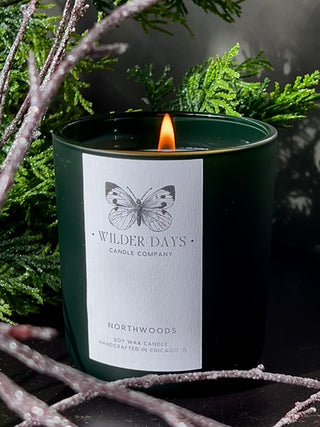 Wilder Days candle with a butterfly design on a label, surrounded by greenery.