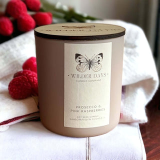 Pink soy candle in a glass jar labeled "Prosecco & Pink Raspberries," styled with soft romantic lighting and raspberry accents.